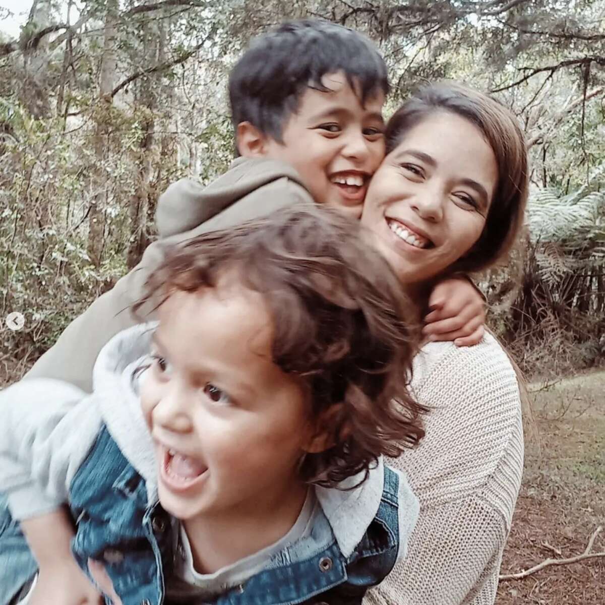Amy and her sons in a park smiling and mid-laugh. Amy and her sons are wearing casual clothes and mid hugging each other while laughing they are part Māori.