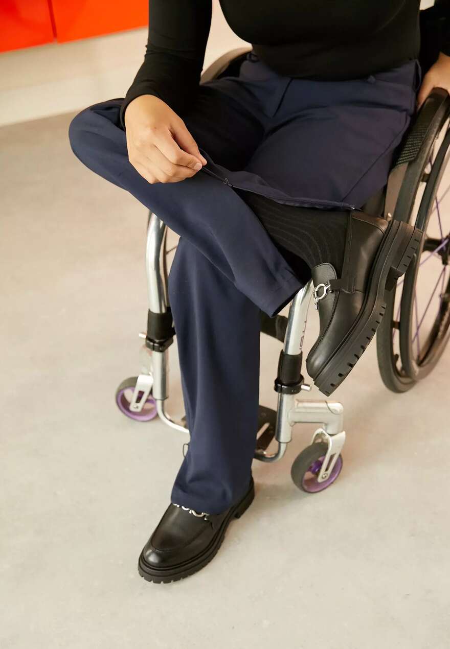 Image shows trouser legs opening wide, to be adaptive. the trousers are navy and straight legged.