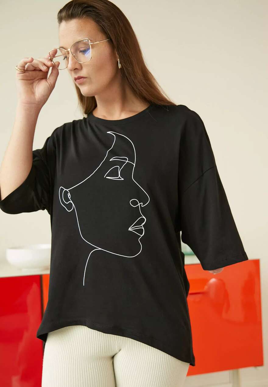 Image is of a woman with fair skin and brown hair, she wears clear rimmed glasses and is an upper limb amputee, her shirt has the outline of a womans face on it.