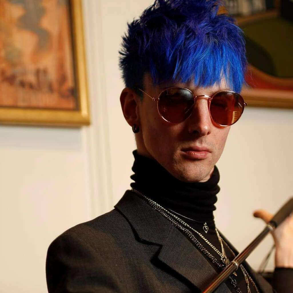 Ari has blue hair, sunglasses and holds his cane