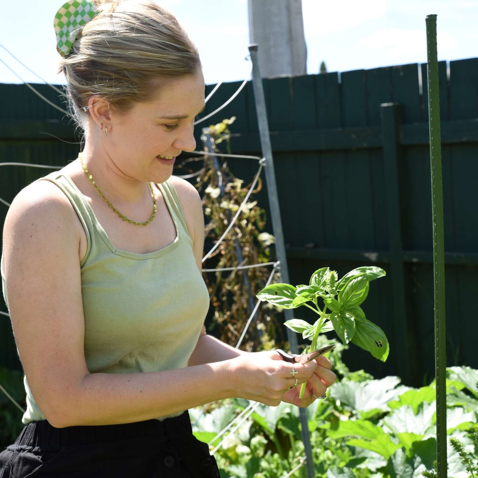 Ellen is a fair-skinned blond female with her hair tied back. She is gardening in a green singlet