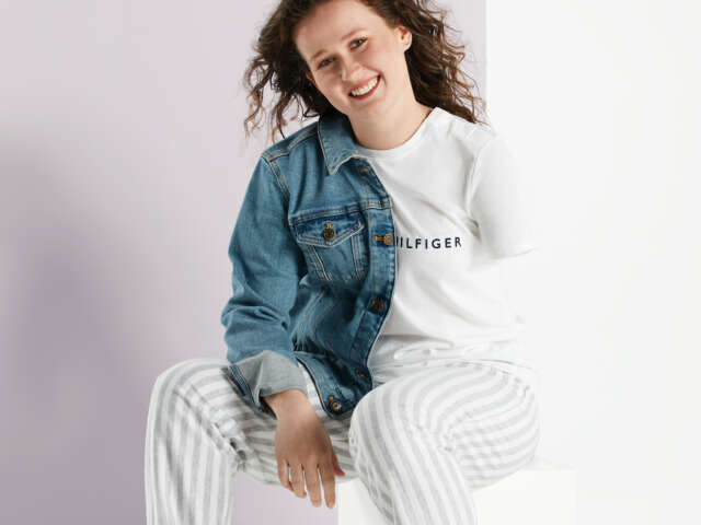 Brylee sits on a stool, she wears a t-shirt and pants with a denim jacket